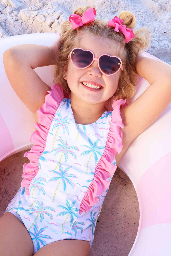 girl laying in inner tube in neon palm tree one piece swimsuit with bright pink ruffles along the front and shoulders