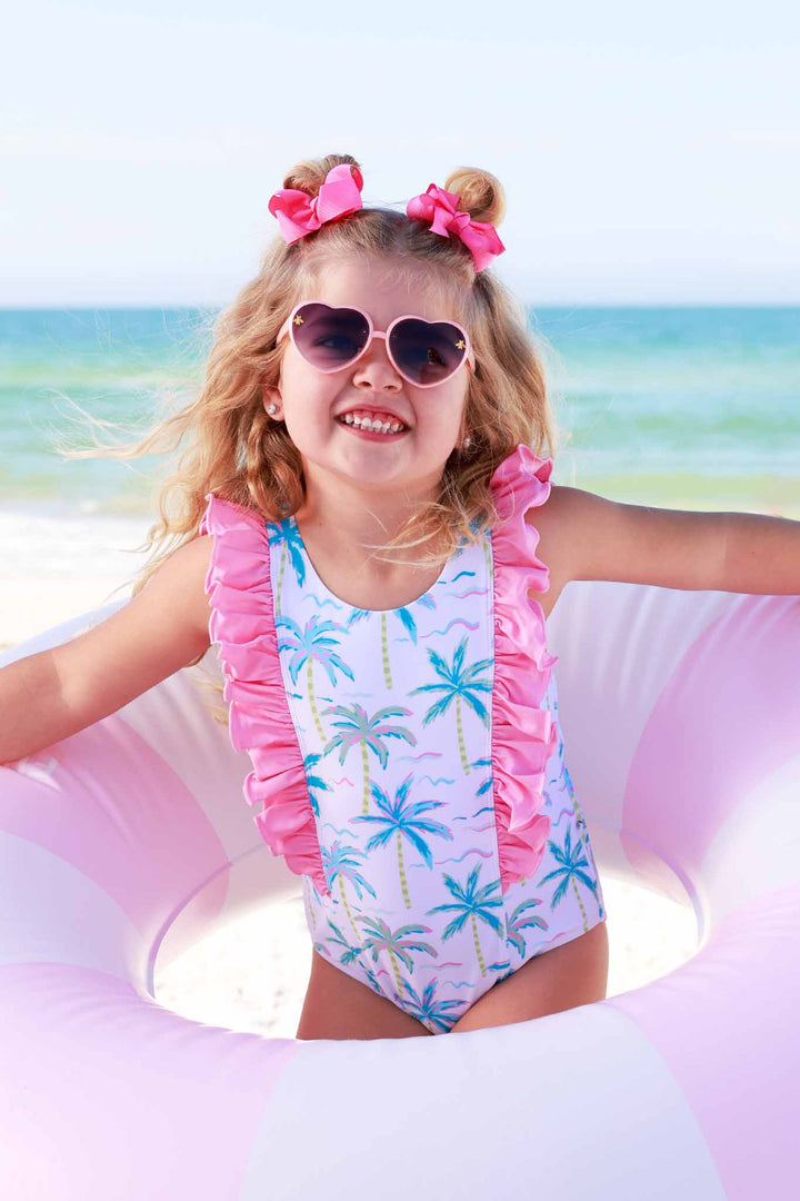 girl standing in inner tube wearing the blue lagoon double ruffle one piece and heart sunglasses