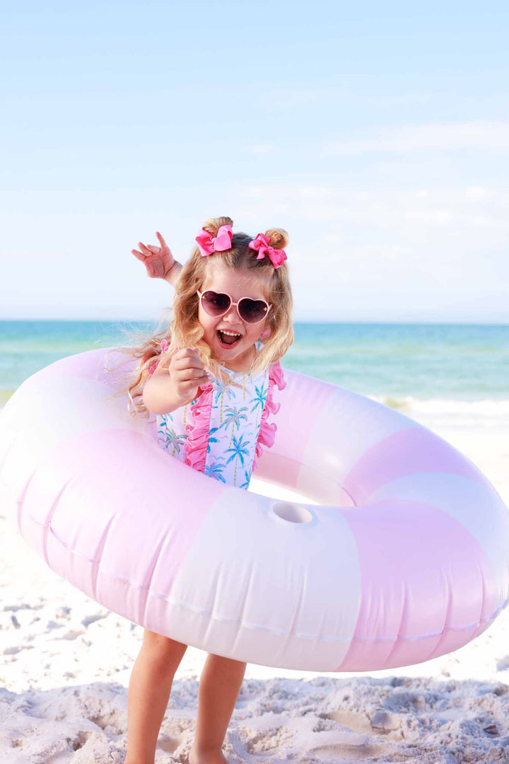 girl playing on beach with pink innertube in blue lagoon double ruffle one piece 
