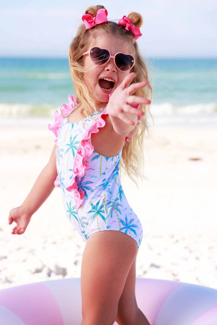 girl playing on beach in palm tree swimsuit with heart sunglasses and space buns with pink bows 