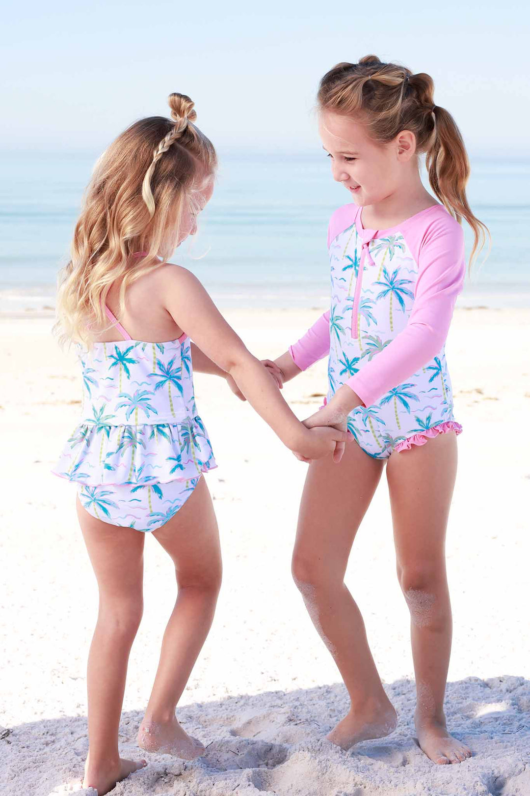 girls twirling on the beach in matching print palm tree swimsuits 