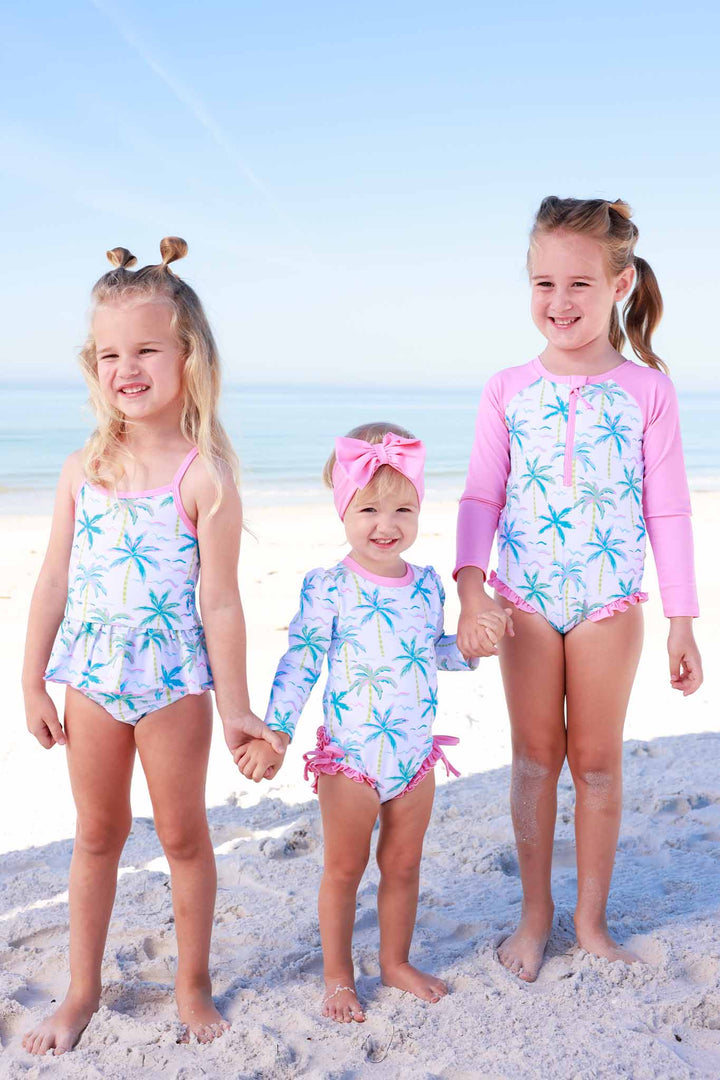sisters holding hands on the beach in blue lagoon matching swimsuits 