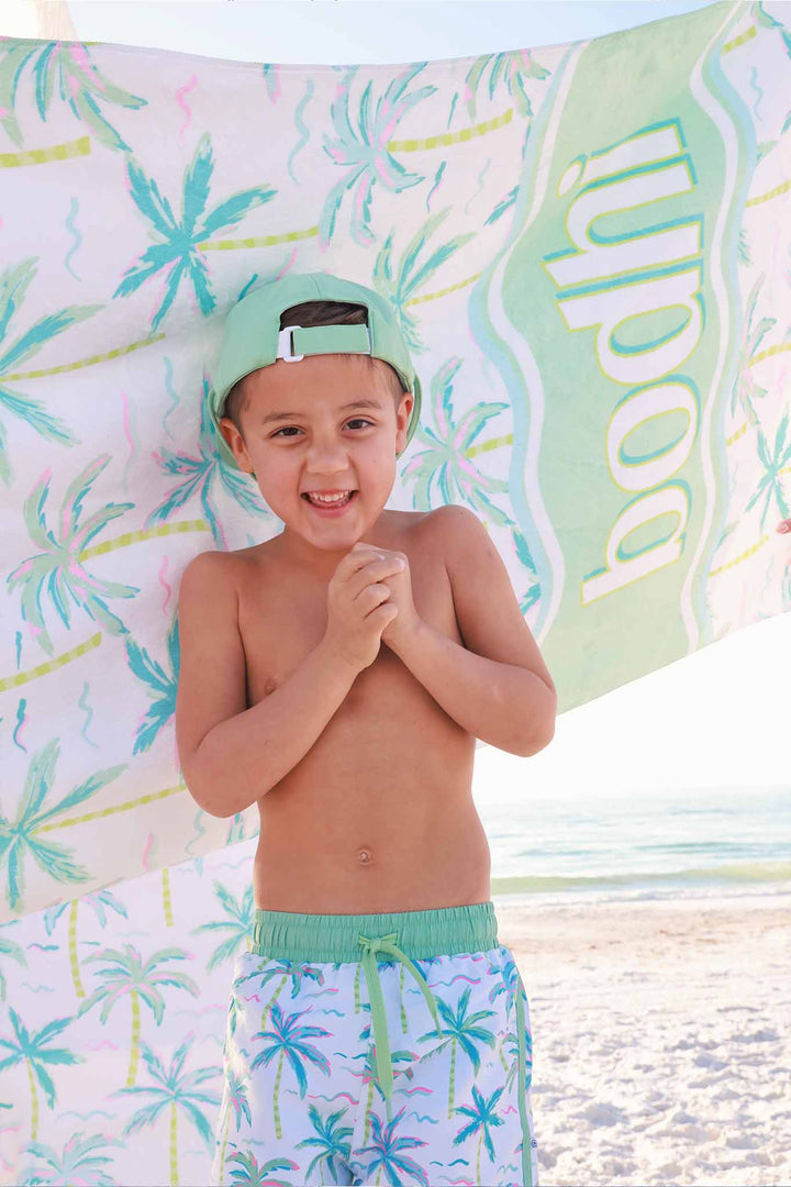boy standing on beach with personalized beach towel behind him with palm trees