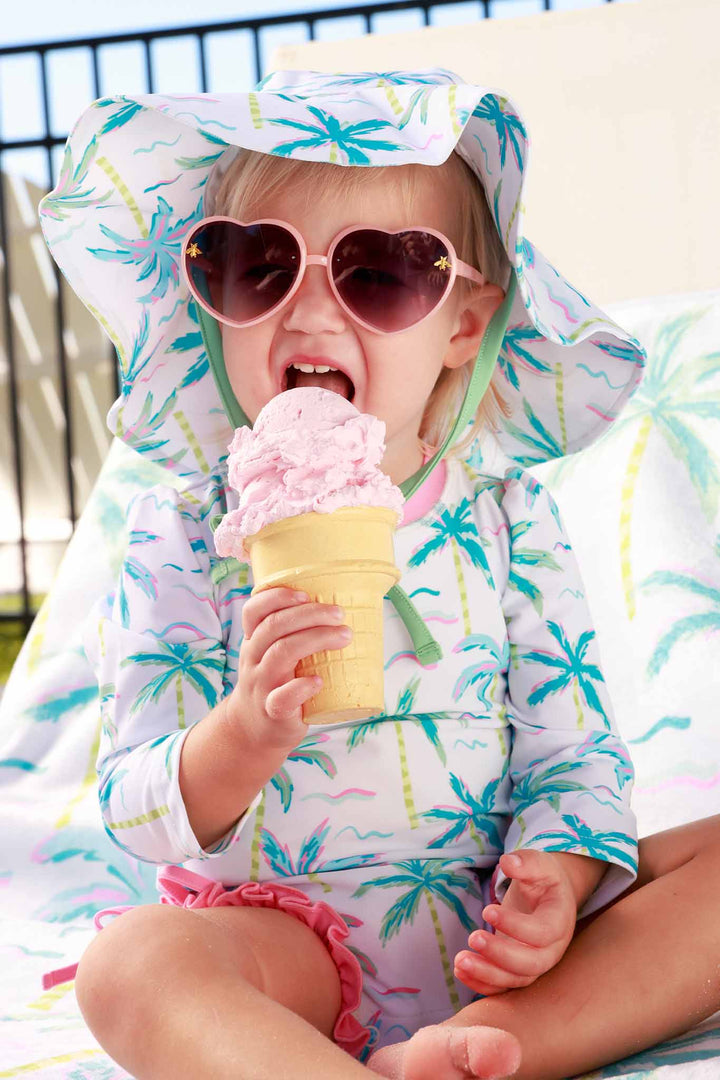girl eating ice cream wearing blue lagoon long sleeve rash guard with ruffle bottom with a matching hat and heart sunglasses