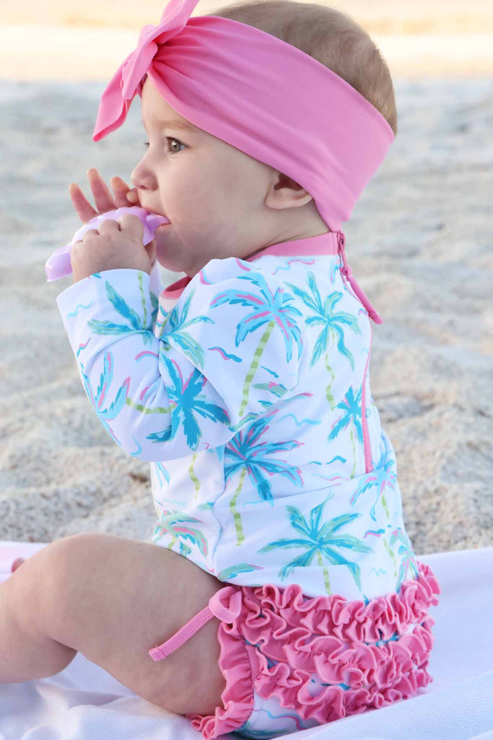 side view of neon palm tree long sleeve rash guard with ruffle bottom with a pink swim bow