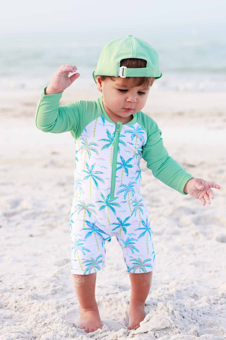 boy walking on beach in neon palm green long sleeve rash guard shortie with matching backwards surf hat 