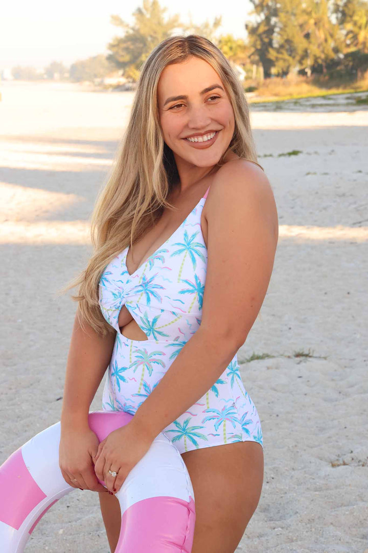 woman wearing neon palm tree cutout one piece swimsuit holding an innertube 