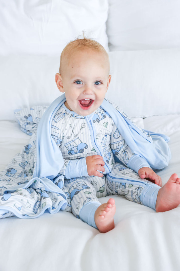 boy sitting on bed in caddie crew pajama romper with blanket over shoulders