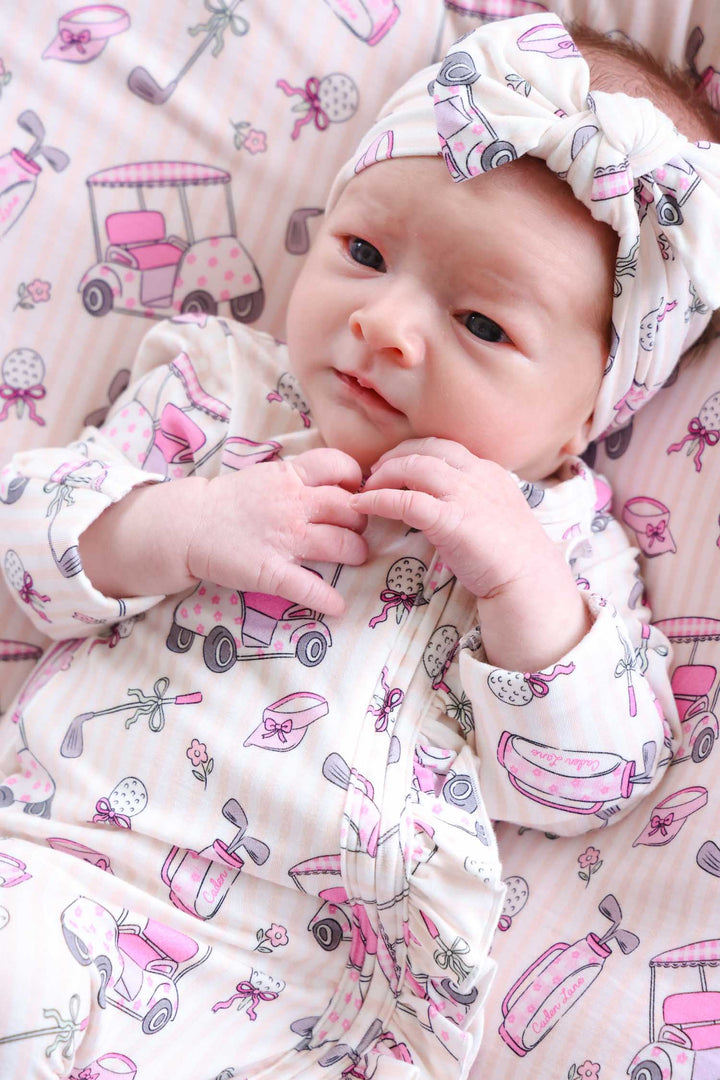 baby girl wearing pink caddie crew ruffle zipper footie with matching headwrap
