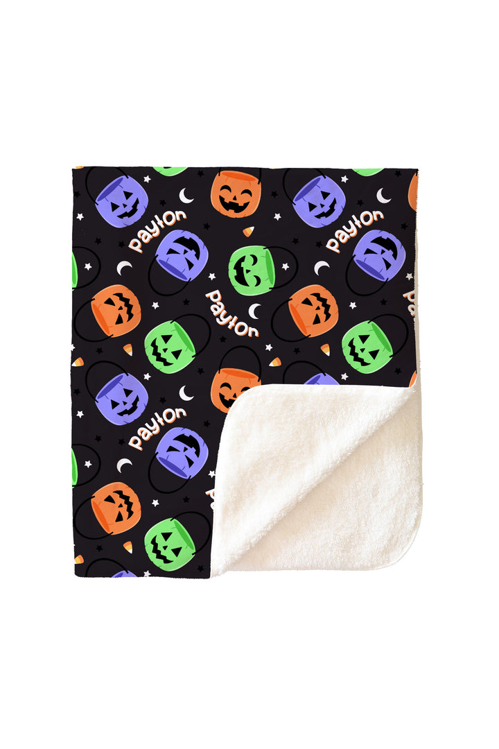 Personalized Halloween sherpa blanket corner folded to show soft cream fleece backing beneath the colorful jack-o-lantern print and name text