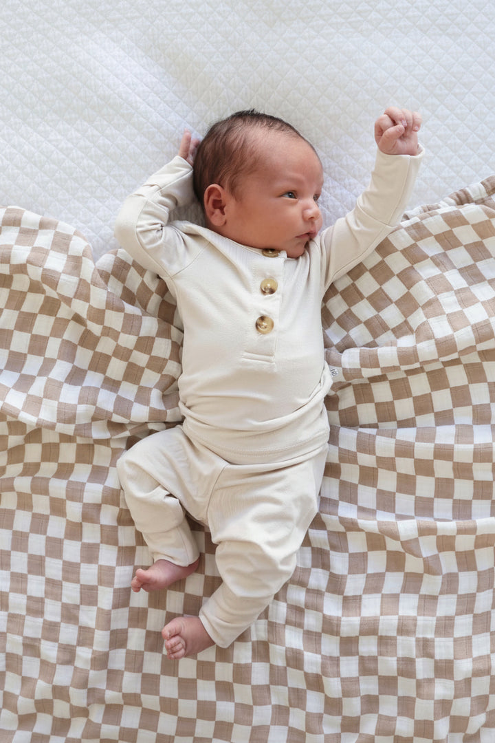 Baby in a Caden Lane cream outfit lying on a checkered blanket
