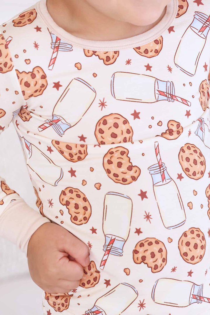 beige pajama set for kids with cookies, jars of milk with a red and white striped straw and black stars
