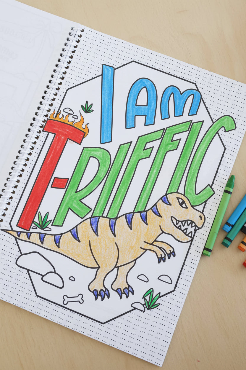 I Am T-Rrific' dinosaur page from a Caden Lane coloring book, partially colored with a yellow and blue T-Rex illustration, surrounded by crayons.