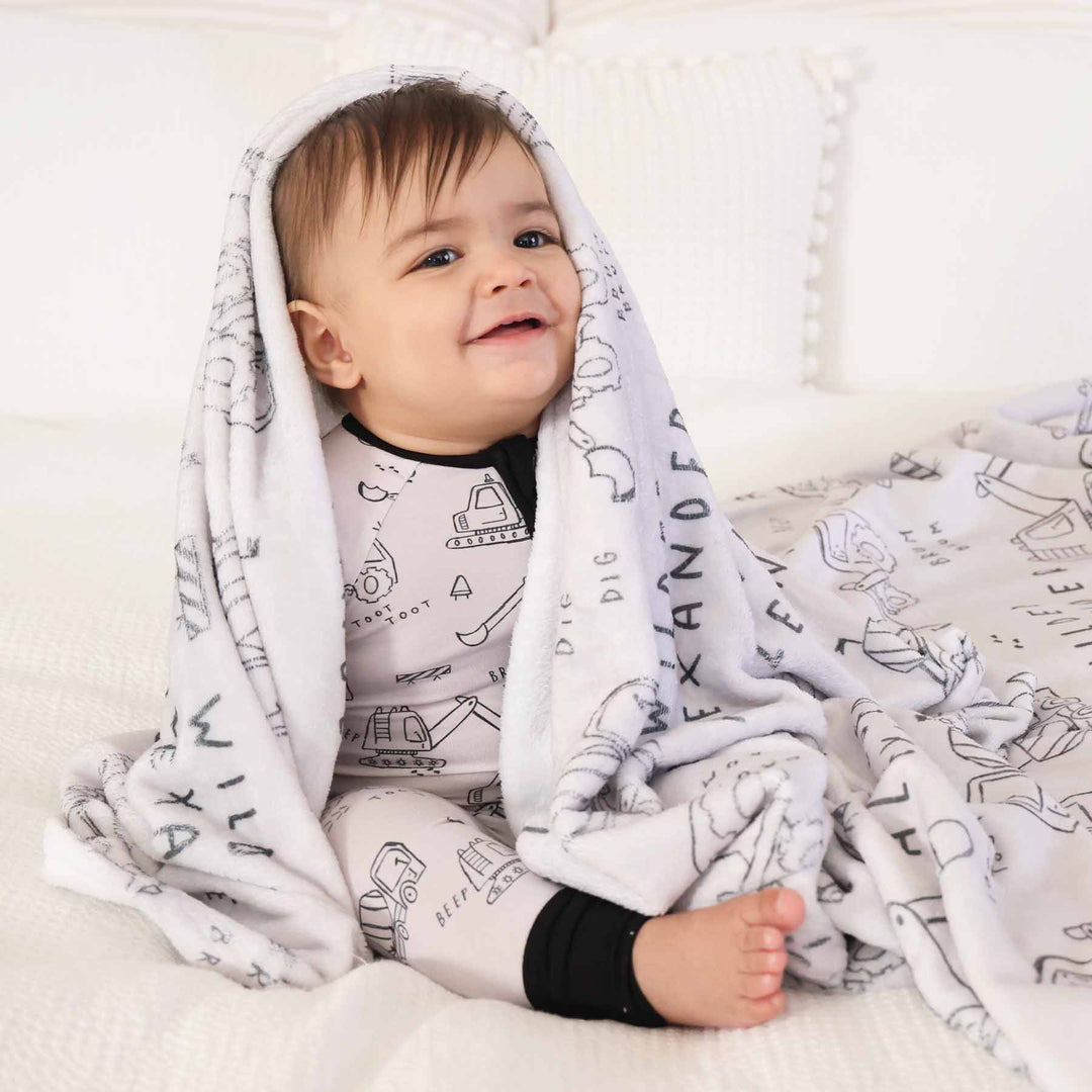 boy with personalized graphic blanket in construction truck print and matching printed sleep romper