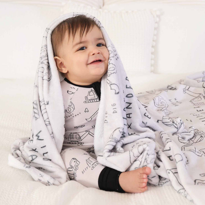 boy with personalized graphic blanket in construction truck print and matching printed sleep romper