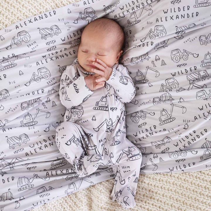 newborn baby with personalized swaddle in construction truck and dozer doodle print with matching zip footie romper