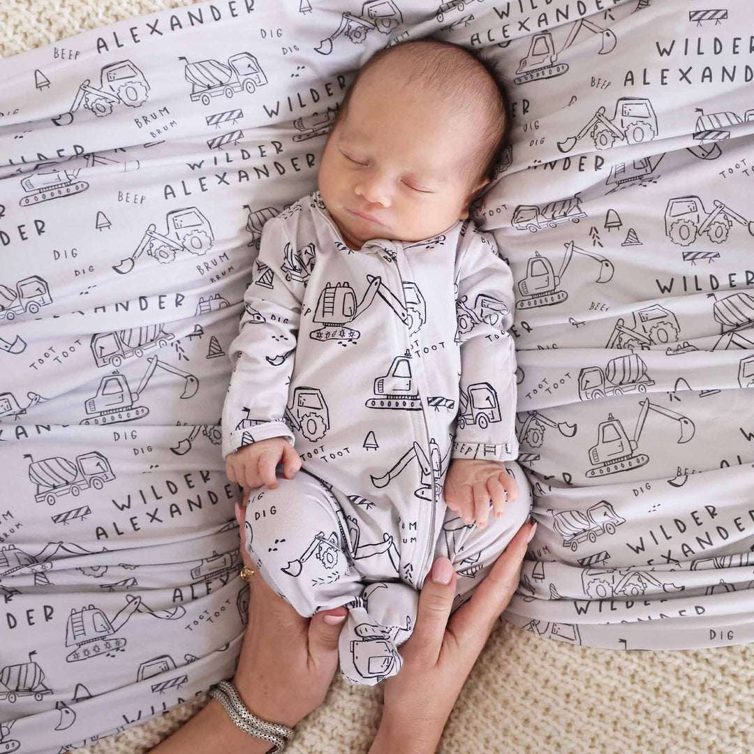 newborn baby boy with personalized swaddle in doodle truck print with matching zip footie romper