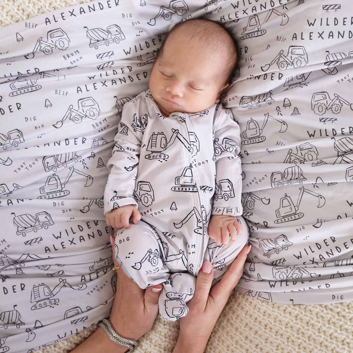 newborn baby boy with personalized swaddle in doodle truck print with matching zip footie romper