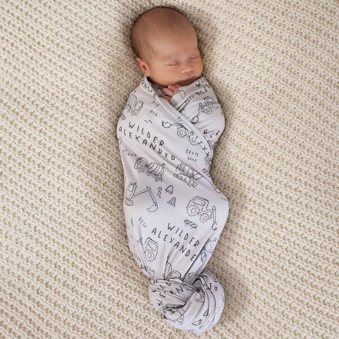 baby in personalized swaddle with construction truck and dozer doodle print