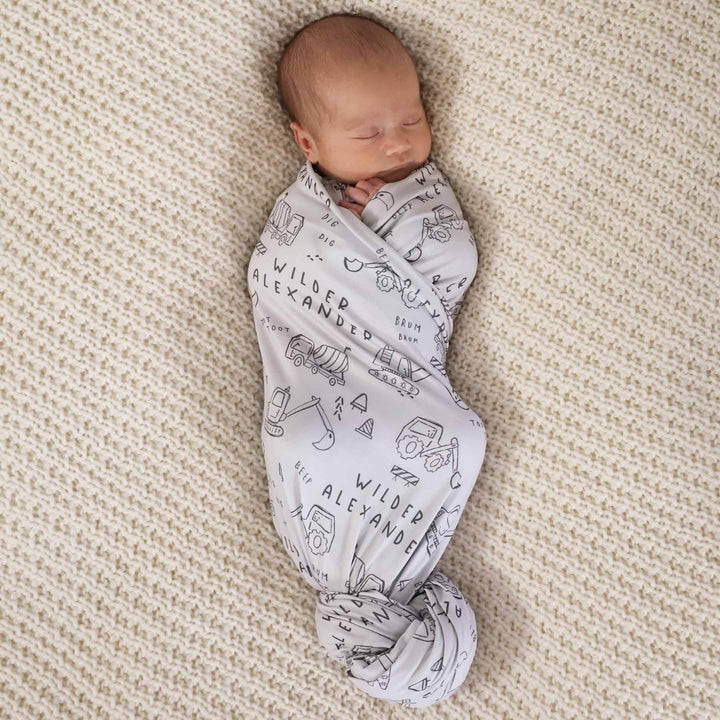 baby in personalized swaddle with construction truck and dozer doodle print