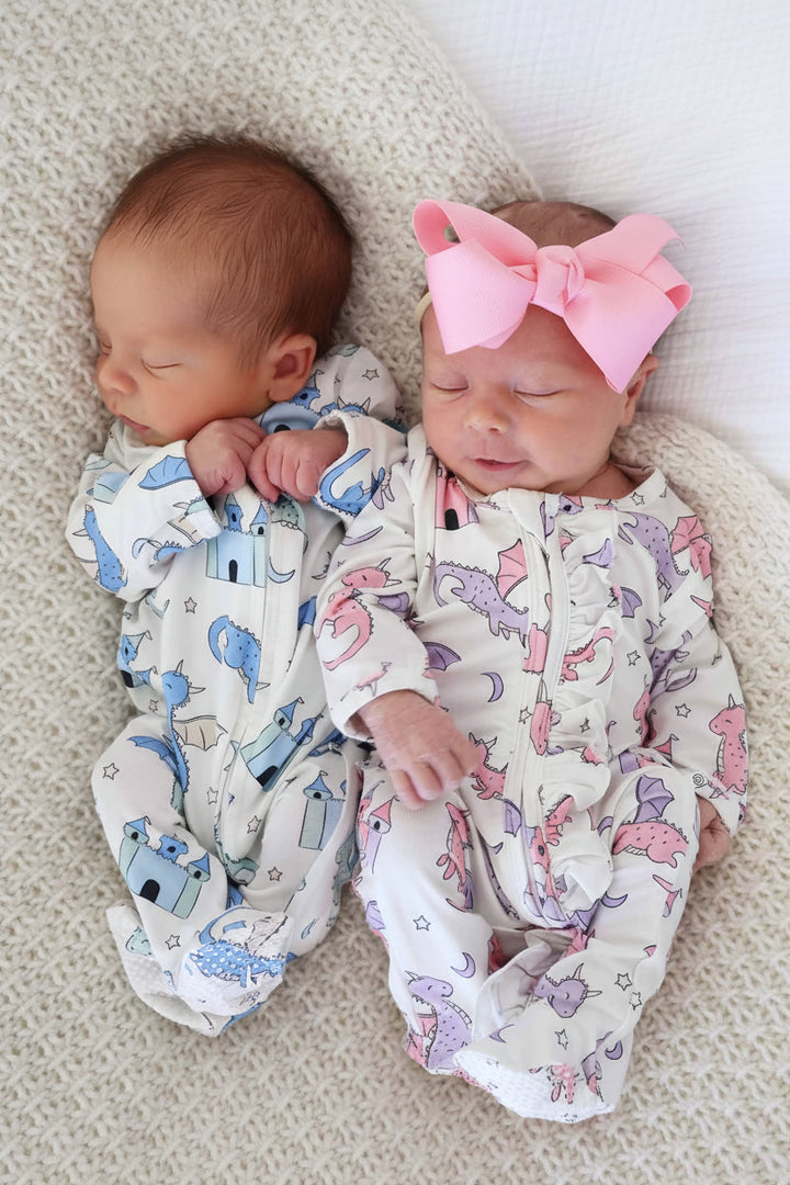 Babies lying on back wearing boy and girl versions of zip-up sleeper with medieval castle pattern