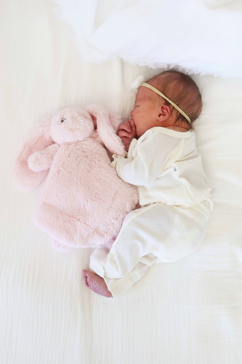 baby laying on side next to a light pink stuffed animal bunny lovey embroidered with name in white thread with script font 