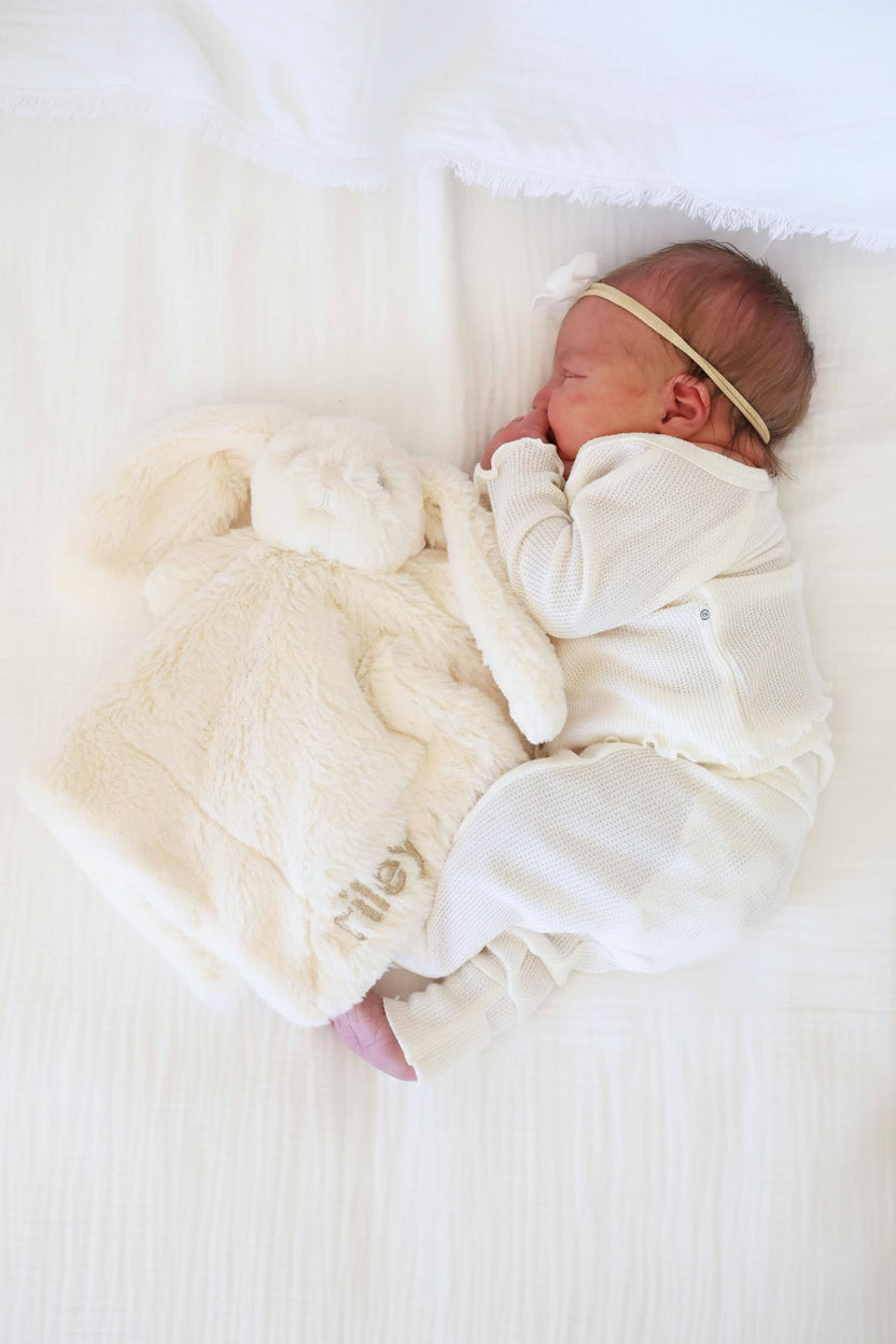 baby laying on side next to a white stuffed bunny lovey embroidered with name 