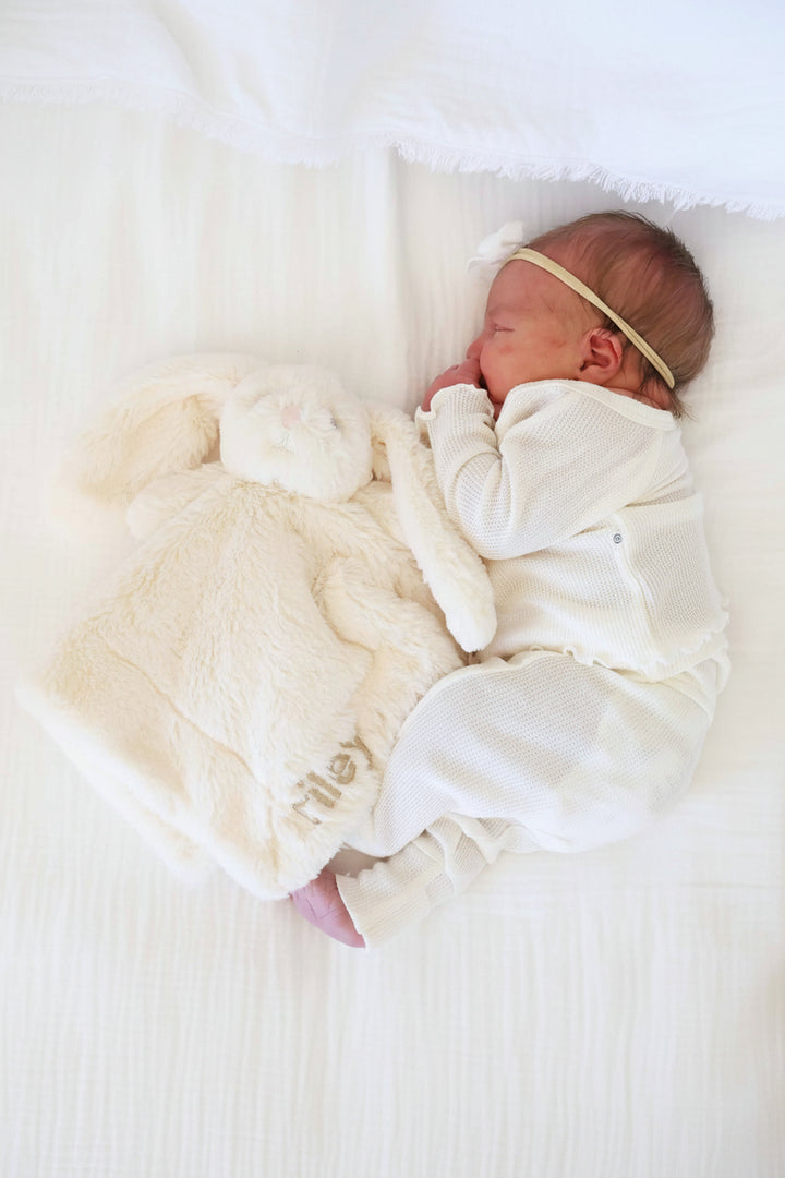 baby laying on side next to a white stuffed bunny lovey embroidered with name 