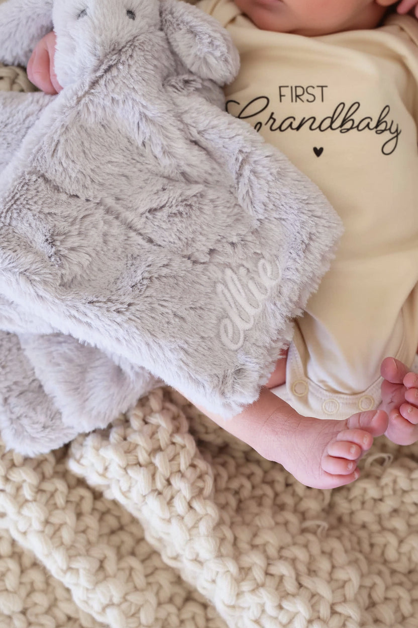 closeup of baby holding a grey elephant plush lovey embroidered with name with white thread in script font 