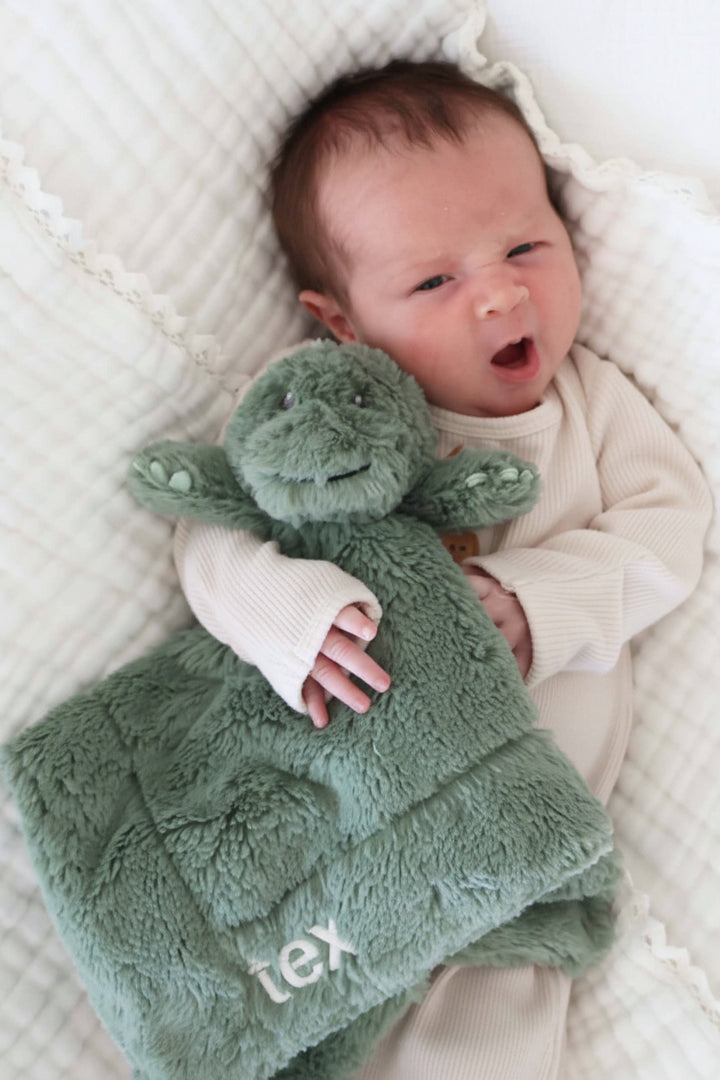 baby in neutral knot gown holding an embroidered dinosaur lovey