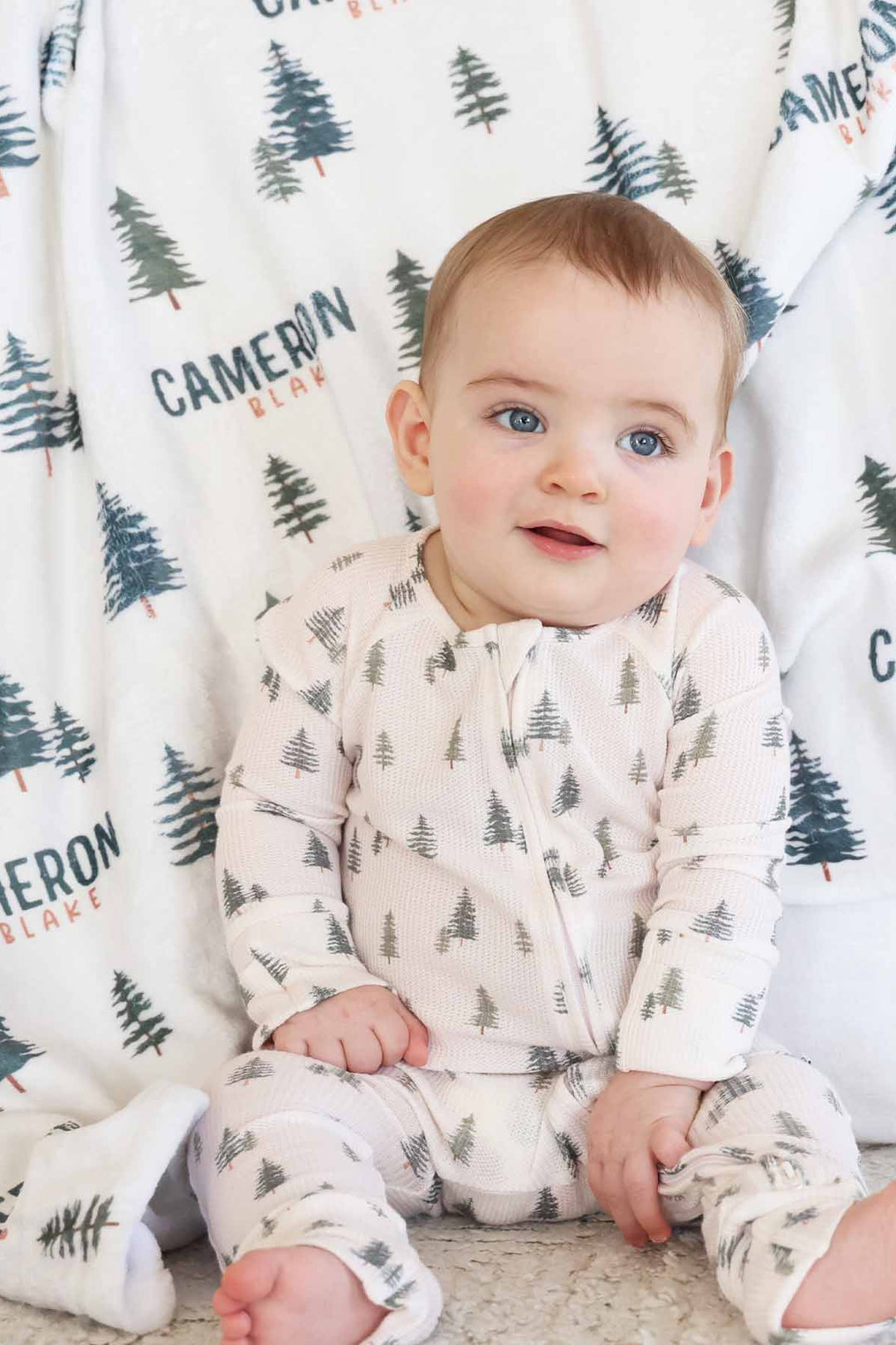 baby wearing evergreen tree bamboo waffle convertible zip romper with matching personalized minky blanket in the background 