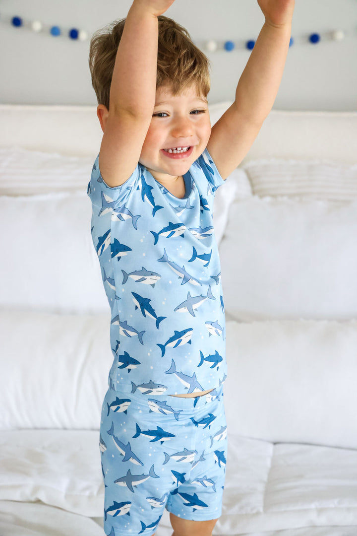 boy with hands up wearing blue shark pajama set 