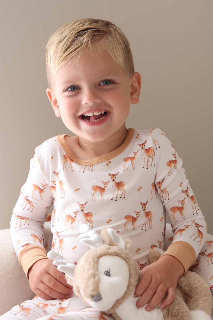 Child dressed in brown and white fawn pajamas cuddling a deer plush toy