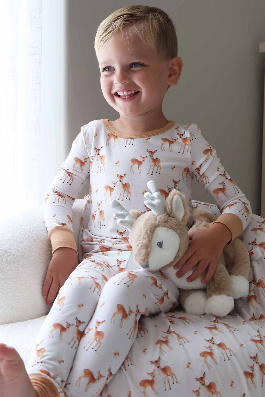 boy wearing a long sleeve fawkn two piece pajama set holding a deer stuffed animal 