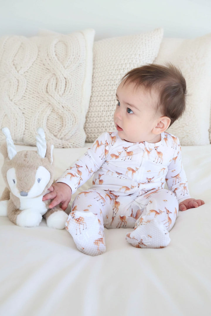 baby sitting on bed in deer zipper footie pajama with deer stuffed animal