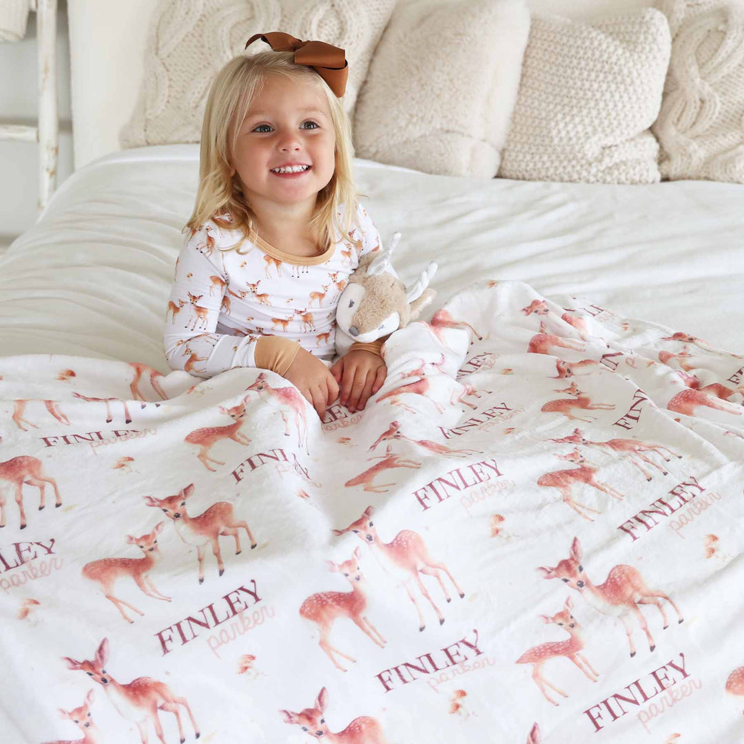 girl wearing neutral deer pajama set with matching personalized blanket for kids 