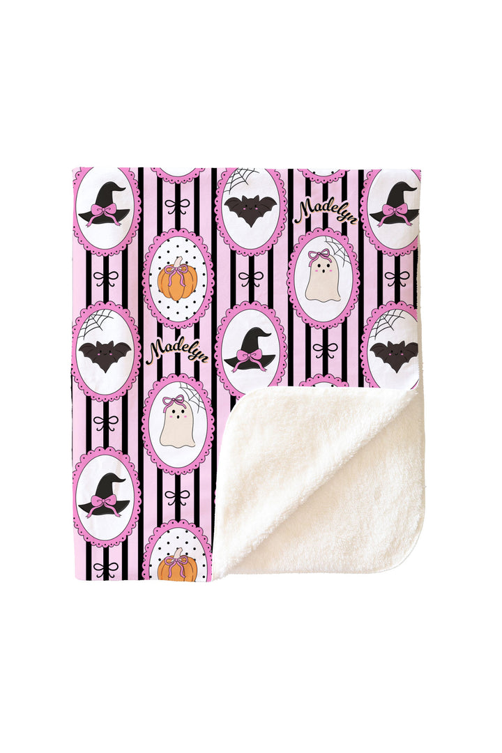 Personalized Halloween blanket showing the folded corner with cream sherpa lining, front side printed with witch hat, bat, ghost, and pumpkin designs and the name 'Madelyn'.