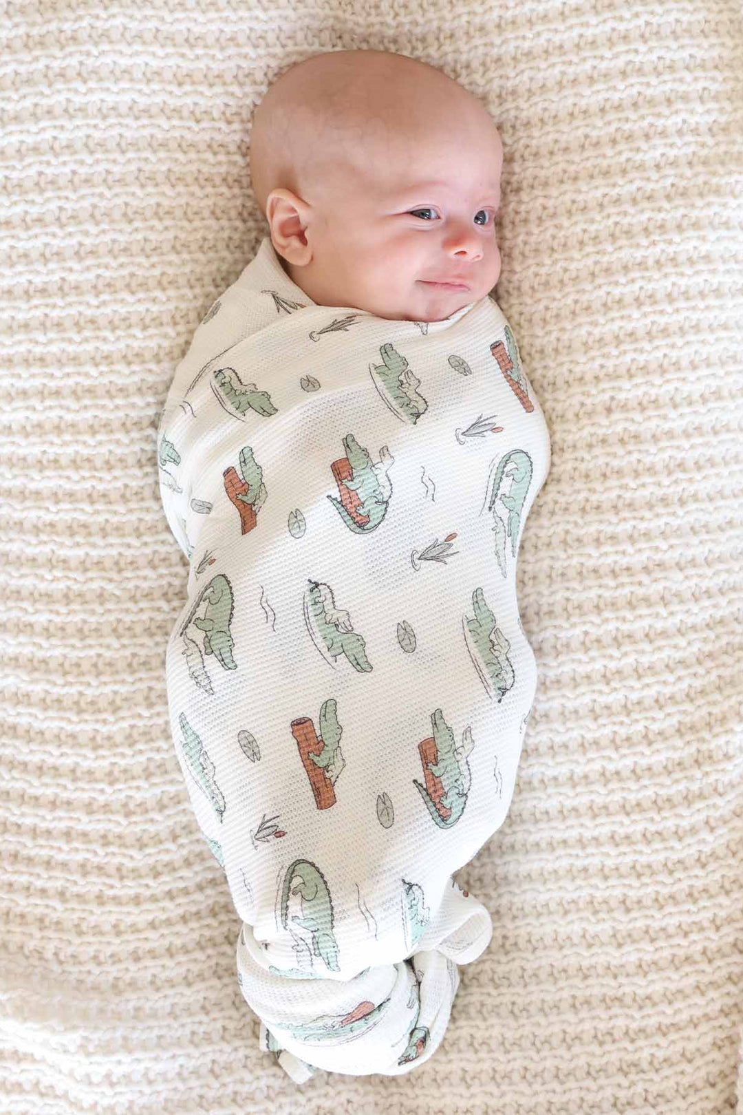 tan swaddle blanket with alligators floating on logs with lily pads and cattails made of bamboo waffle fabric 
