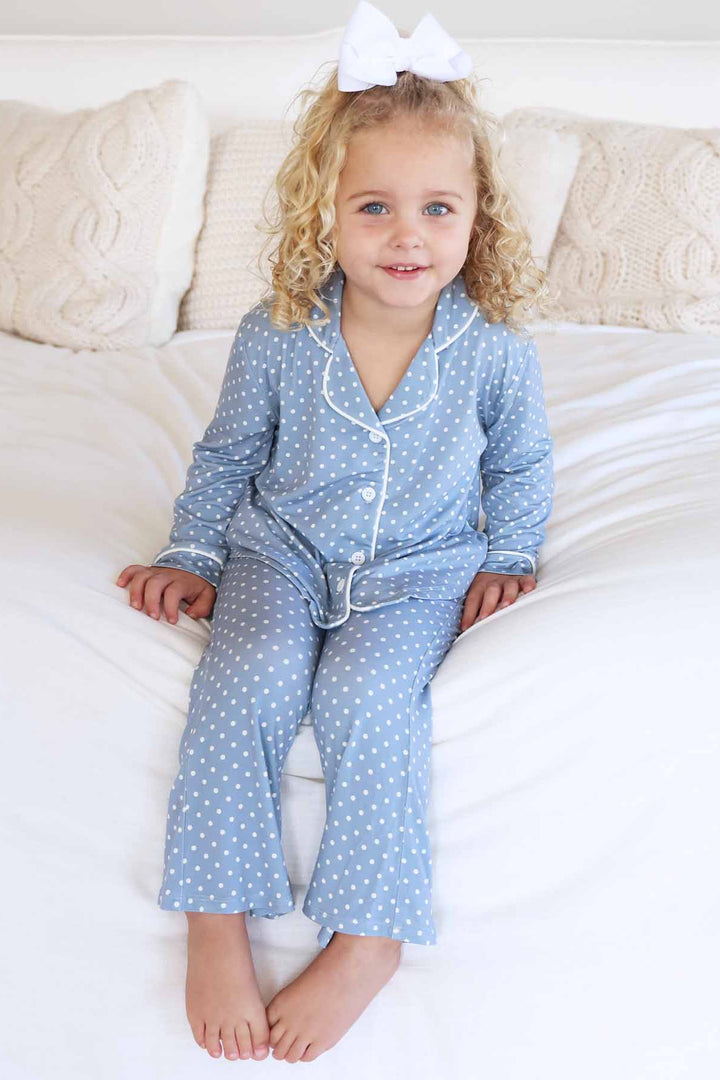 girl sitting on bed wearing a long sleeve collared button up blue lounge set with flare pants that is blue with white polka dots 
