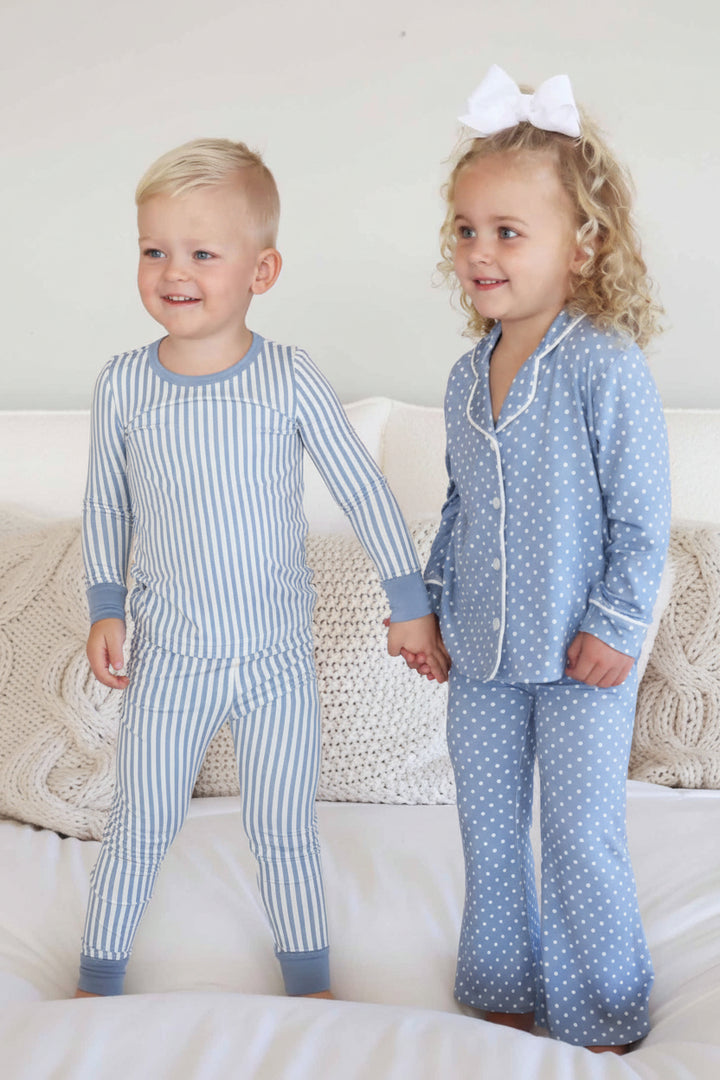 boy wearing a blue and white stripe pajama set holding hands with girls wearing a coordinating long sleeve lounge set that is blue with white polka dots 