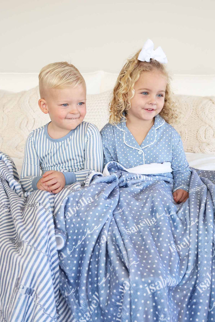 sibling matching pajama and lounge sets. boy is wearing a blue and white stripe long sleeve pajama set and girl is wearing a long sleeve lounge set with polka dots.