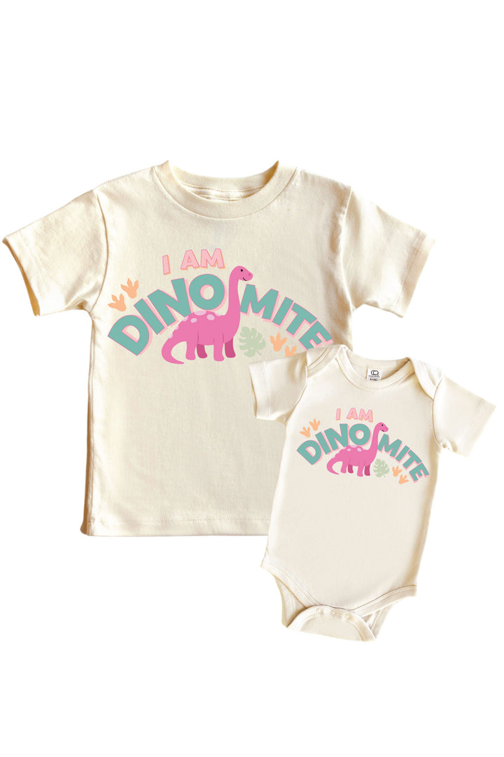 Natural cream kids tee and baby bodysuit set with I AM DINOMITE text in teal and pink lettering featuring a pink brontosaurus dinosaur graphic with colorful leaf accents