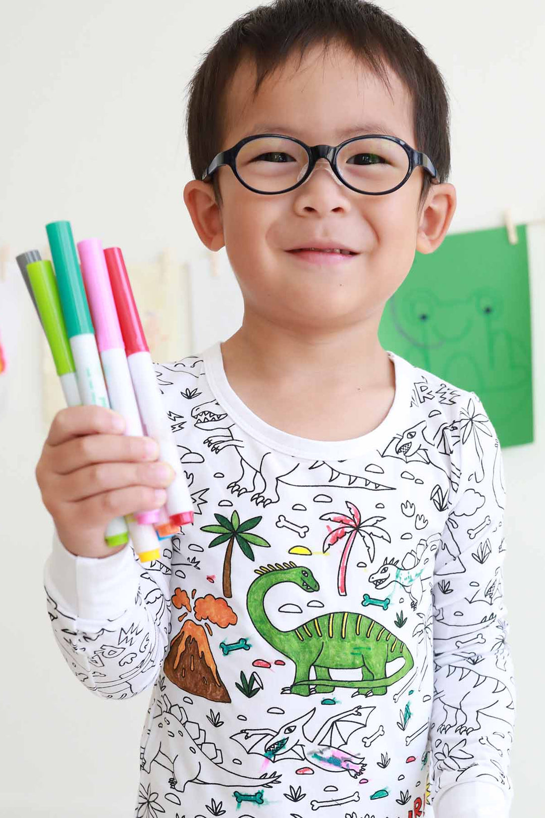 boy wearing Jurassic Playground Colorable Pajama Two Piece Set and holding markers