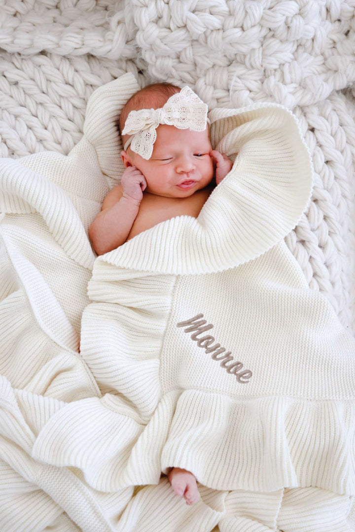 baby wrapped in embroidered ivory blanket with lace bow