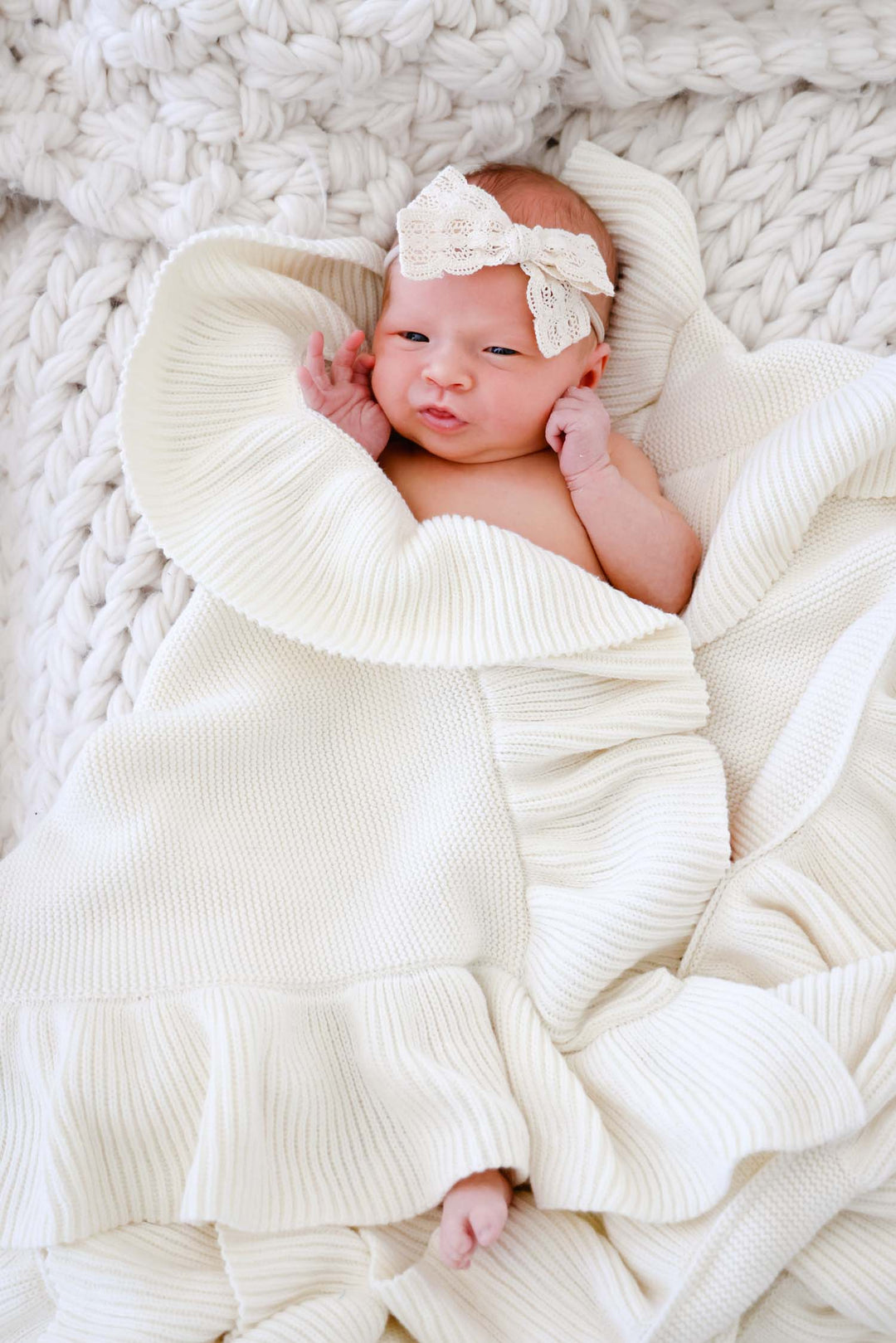 baby wrapped in ivory knit blanket with ivory lace bow on head