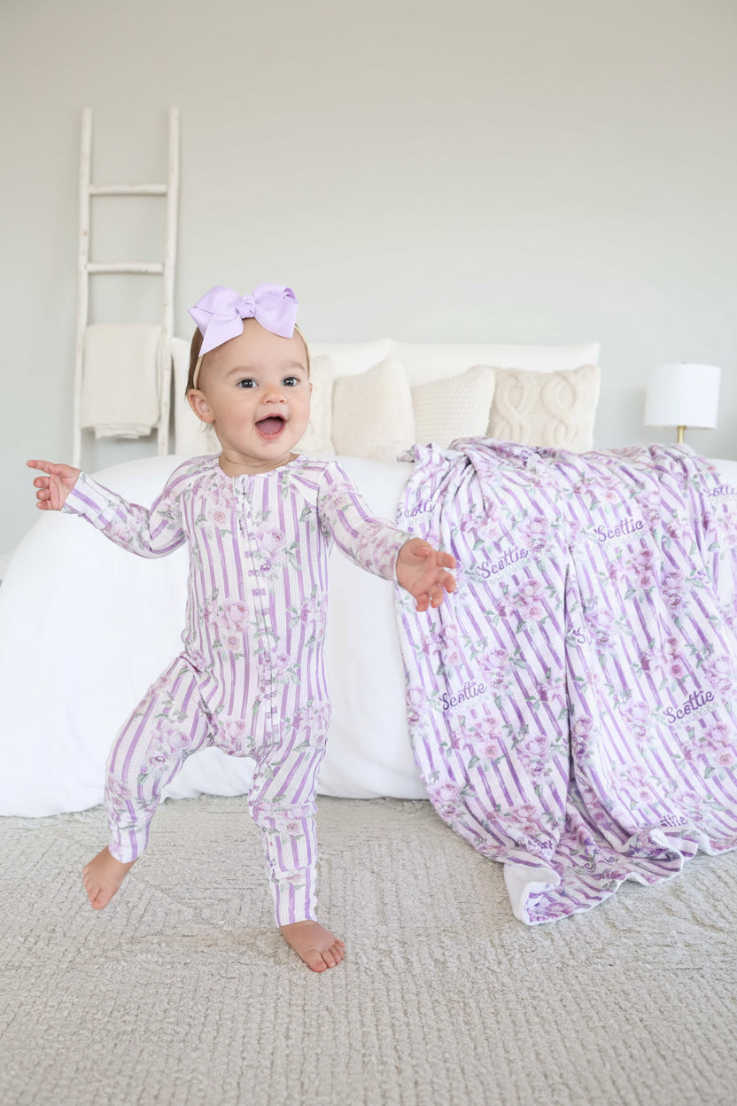 baby girl wearing purple stripe and rose bamboo waffle convertible zip romper with flip mitts and footies with matching blanket in the background 