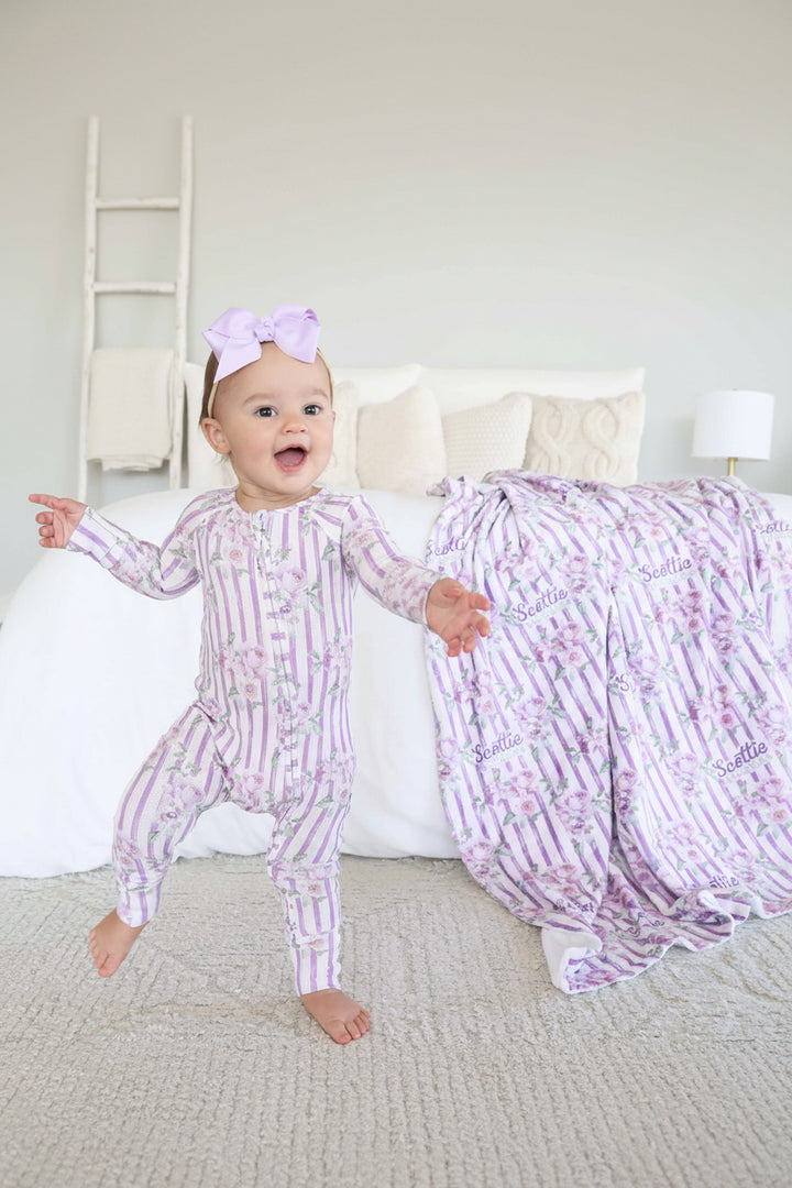 baby girl wearing purple stripe and rose bamboo waffle convertible zip romper with flip mitts and footies with matching blanket in the background 