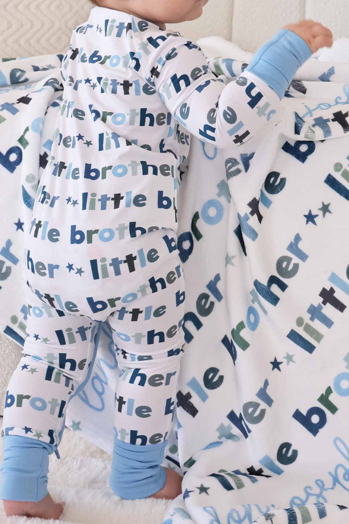 baby wearing the little brother zip romper and standing near matching personalzied blanket