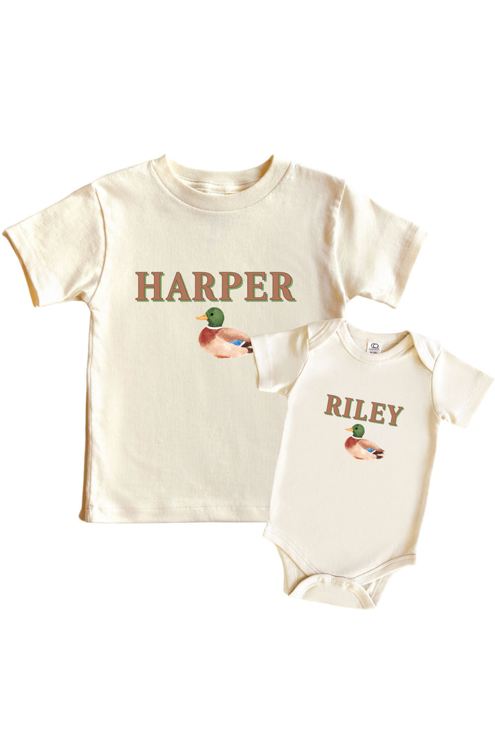 Personalized natural little mallard duck graphic kids tee and baby bodysuit displayed together, each with custom name printed on front