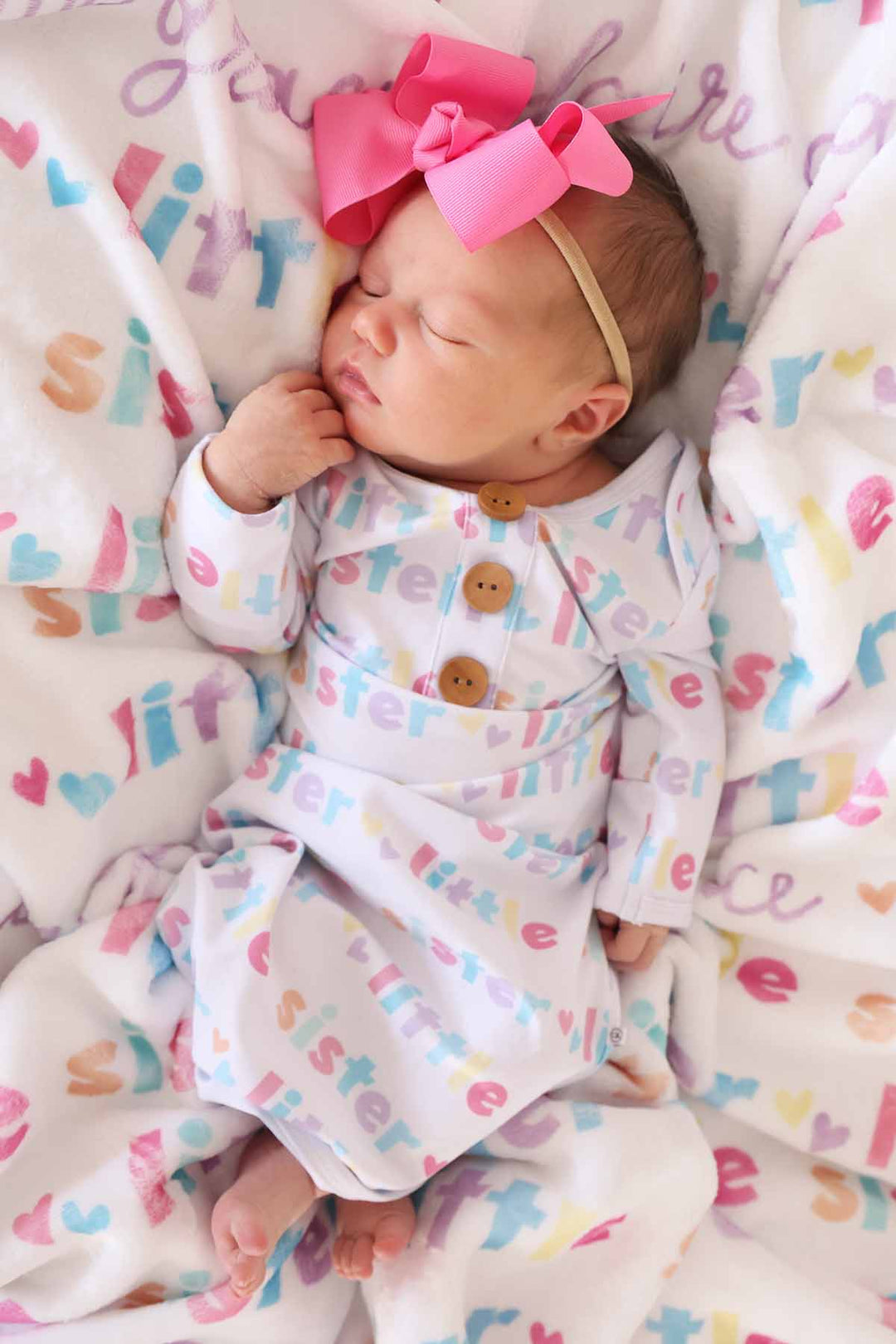 newborn wearing little sister knot gown with pink bow headband